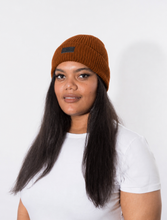 Load image into Gallery viewer, A woman with curly black hair, wearing a rust-orange ribbed knit beanie that is lined with satin for healthy hair care