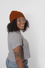 Load image into Gallery viewer, A woman with curly black hair, wearing a rust-orange ribbed knit beanie that is lined with satin for healthy hair care