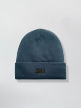 Load image into Gallery viewer, Blue teal Satin Lined beanie with a logo on a light gray background
