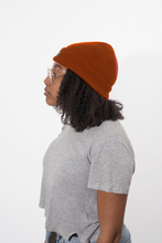 Load image into Gallery viewer, A woman with curly black hair, wearing a rust-orange ribbed knit beanie that is lined with satin for healthy hair care
